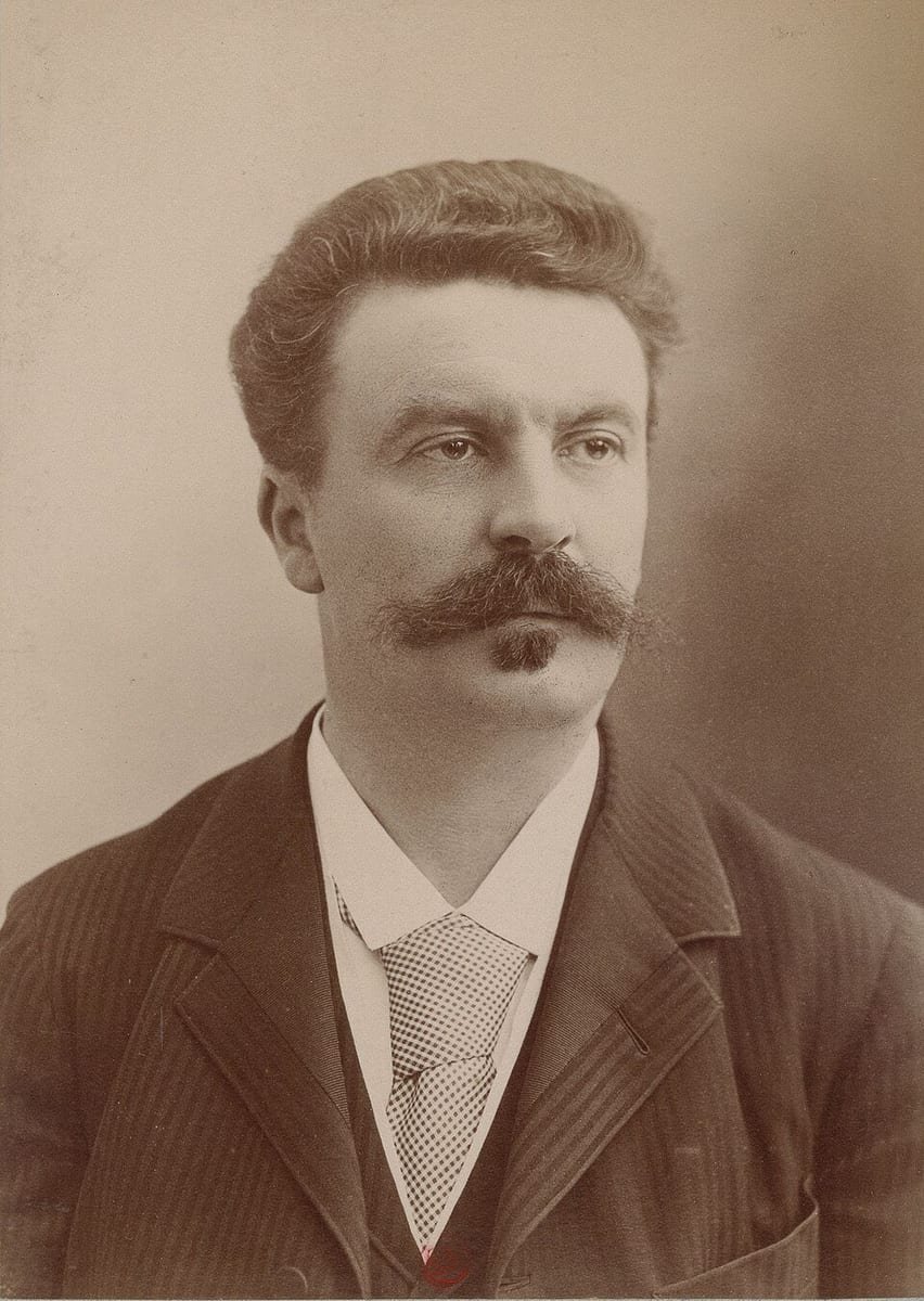 Photographie sépia d'un homme robuste aux cheveux bruns, à grosse moustache et petite barbiche, en veston rayé