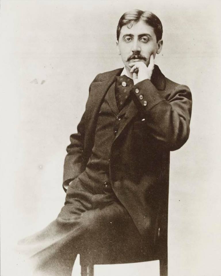 Photographie d'un jeune homme élégant à moustache, assis de biais sur une chaise, la main droite sous le menton