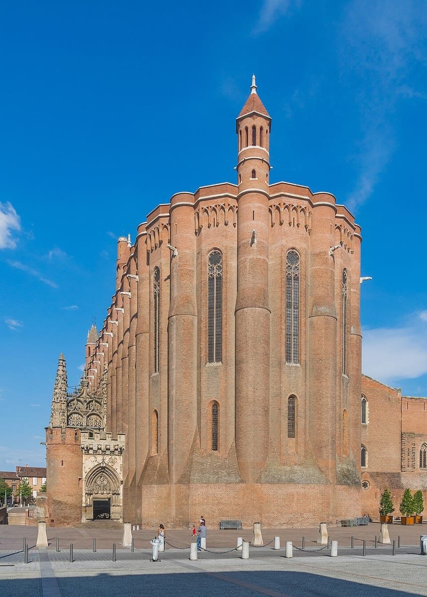 Chevet massif d'une cathédrale en briques rouges, aux murs arrondis comme des tours, sous un ciel bleu