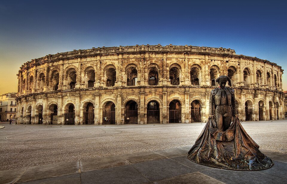 Amphithéâtre romain de pierre à deux étages d'arcades, au coucher du soleil, avec une statue de torero au premier plan