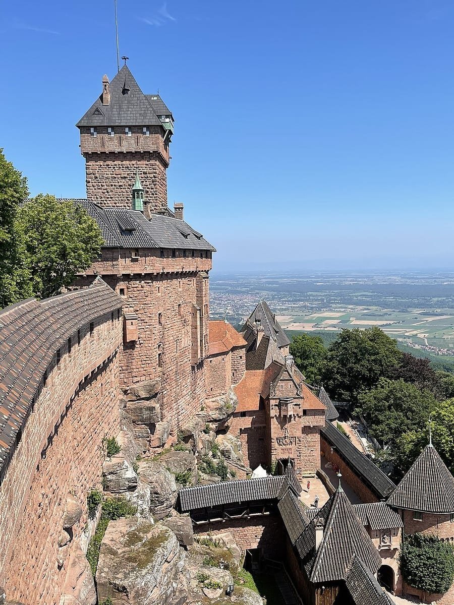 Château fort de grès rose avec un haut donjon carré, perché sur un éperon rocheux au-dessus d'une vaste plaine