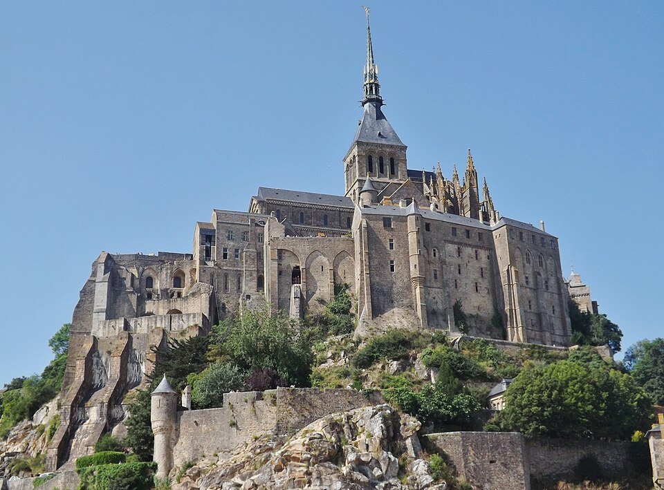 Vue d'une abbaye perchée sur un rocher, avec une flèche élancée