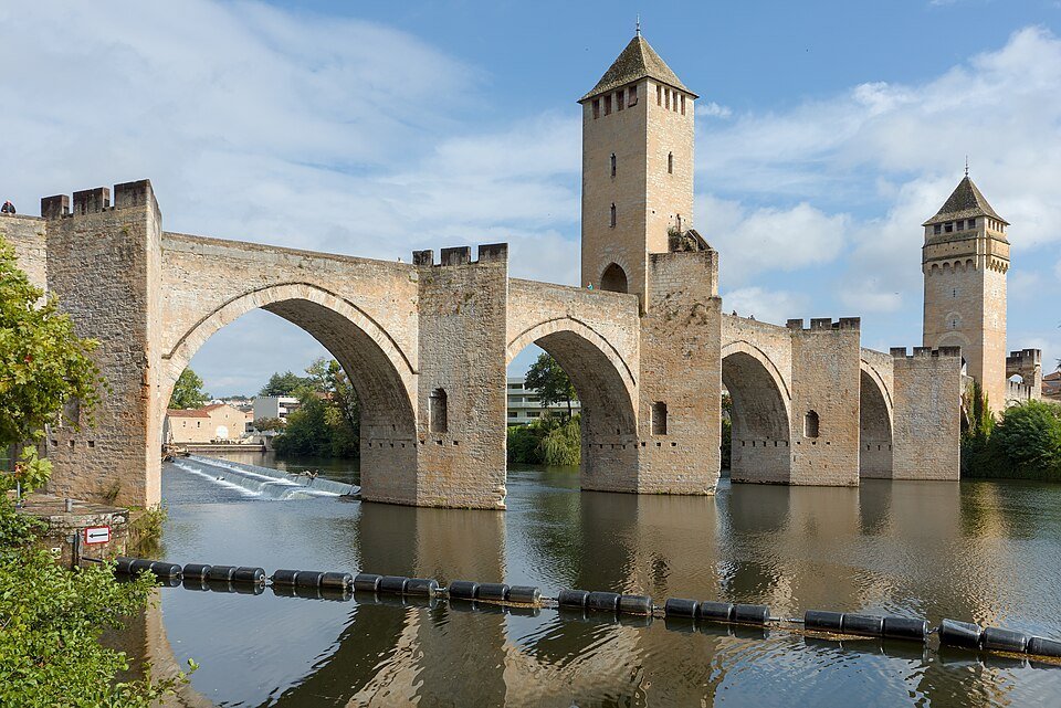Pont médiéval de pierre à grandes arches surmonté de trois tours carrées, au-dessus d'une rivière
