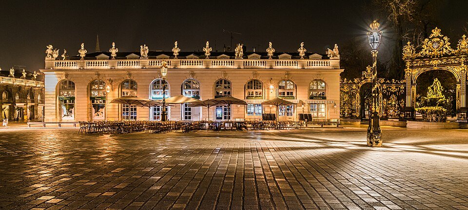 Place bordée de bâtiments classiques illuminés la nuit, grilles dorées
