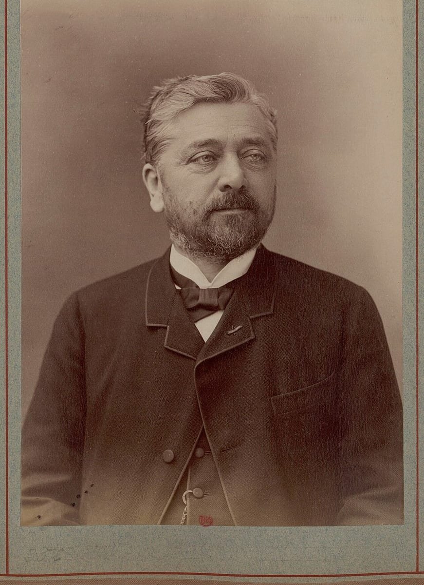 Photographie sépia d'un homme aux cheveux gris et à la barbe courte, en redingote et nœud papillon